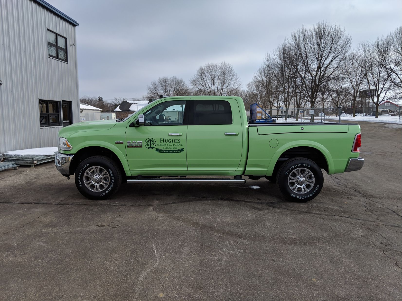 A green ram truck is parked in front of a building.
