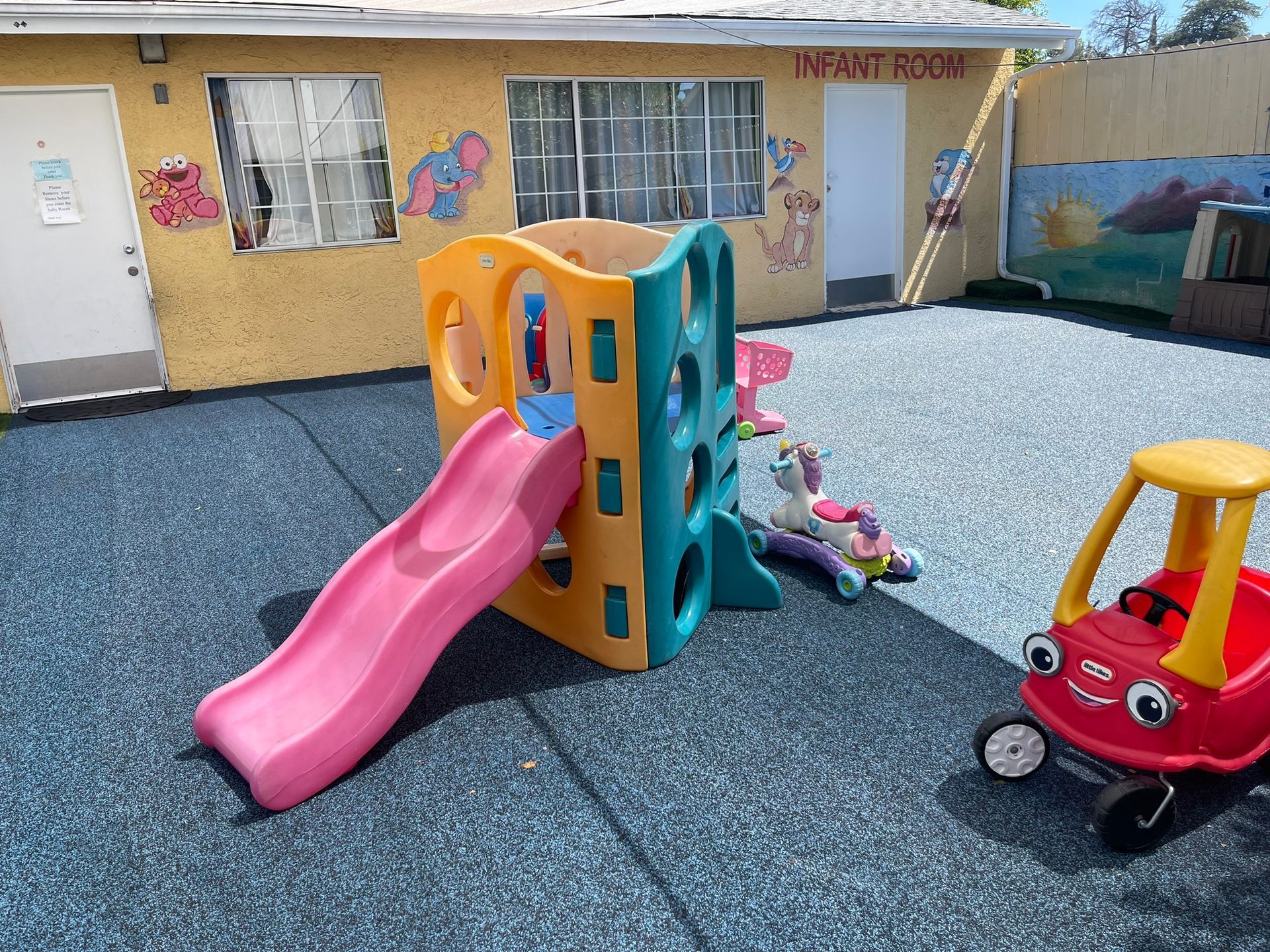 A children 's playground with a pink slide and a red toy car.