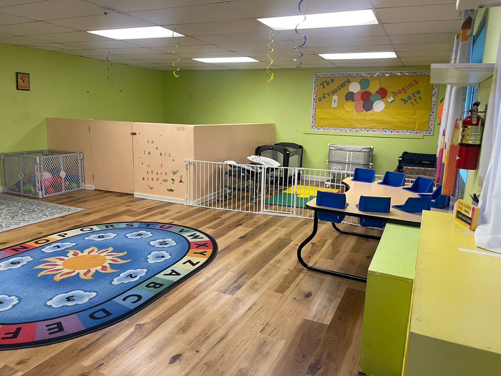 A classroom with a table and chairs and a rug with the alphabet on it.