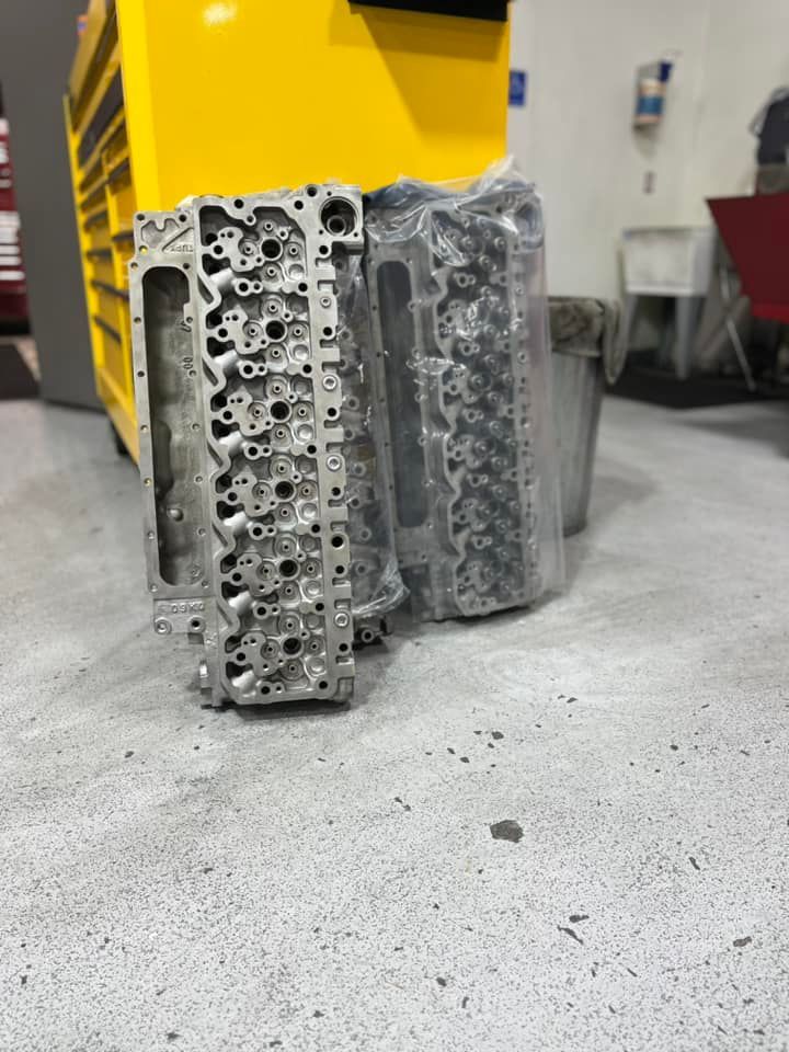 Two metal engine cylinder heads stand upright on a concrete workshop floor in front of a yellow tool chest.