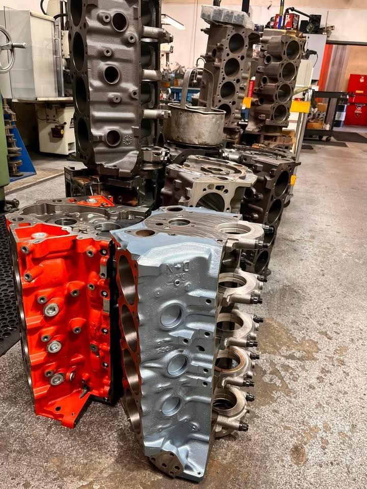 A collection of assorted automotive engine blocks in a workshop, featuring various finishes like bright orange and grey.