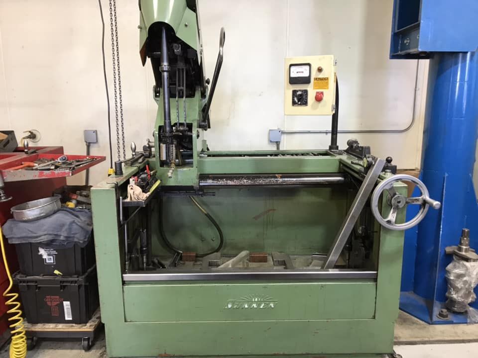 A green industrial machine for metal surfacing or grinding in a workshop, featuring a control box and a hand wheel.