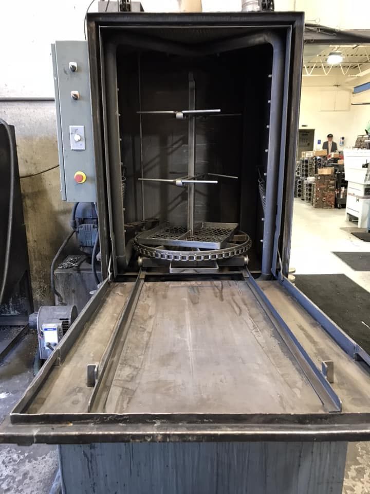 An industrial batch oven with an open door, metal tracks on the floor, and a rotating rack mechanism inside.