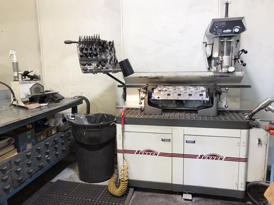 A metal engine cylinder head sits in a Sunnen machine for resurfacing in a workshop.