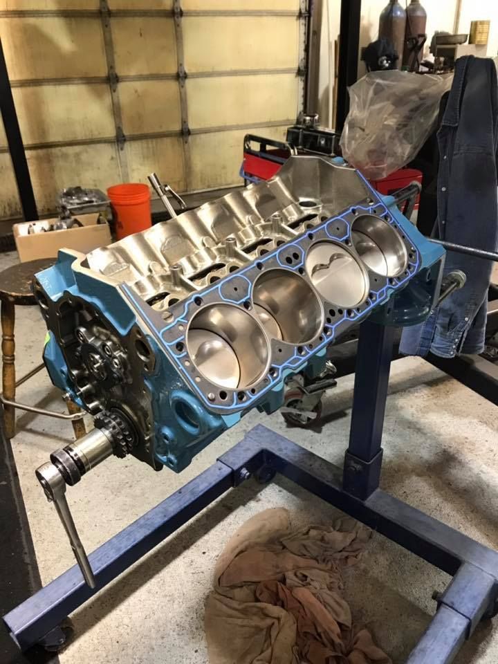 A light blue engine block sits mounted on a rotating engine stand inside a workshop.