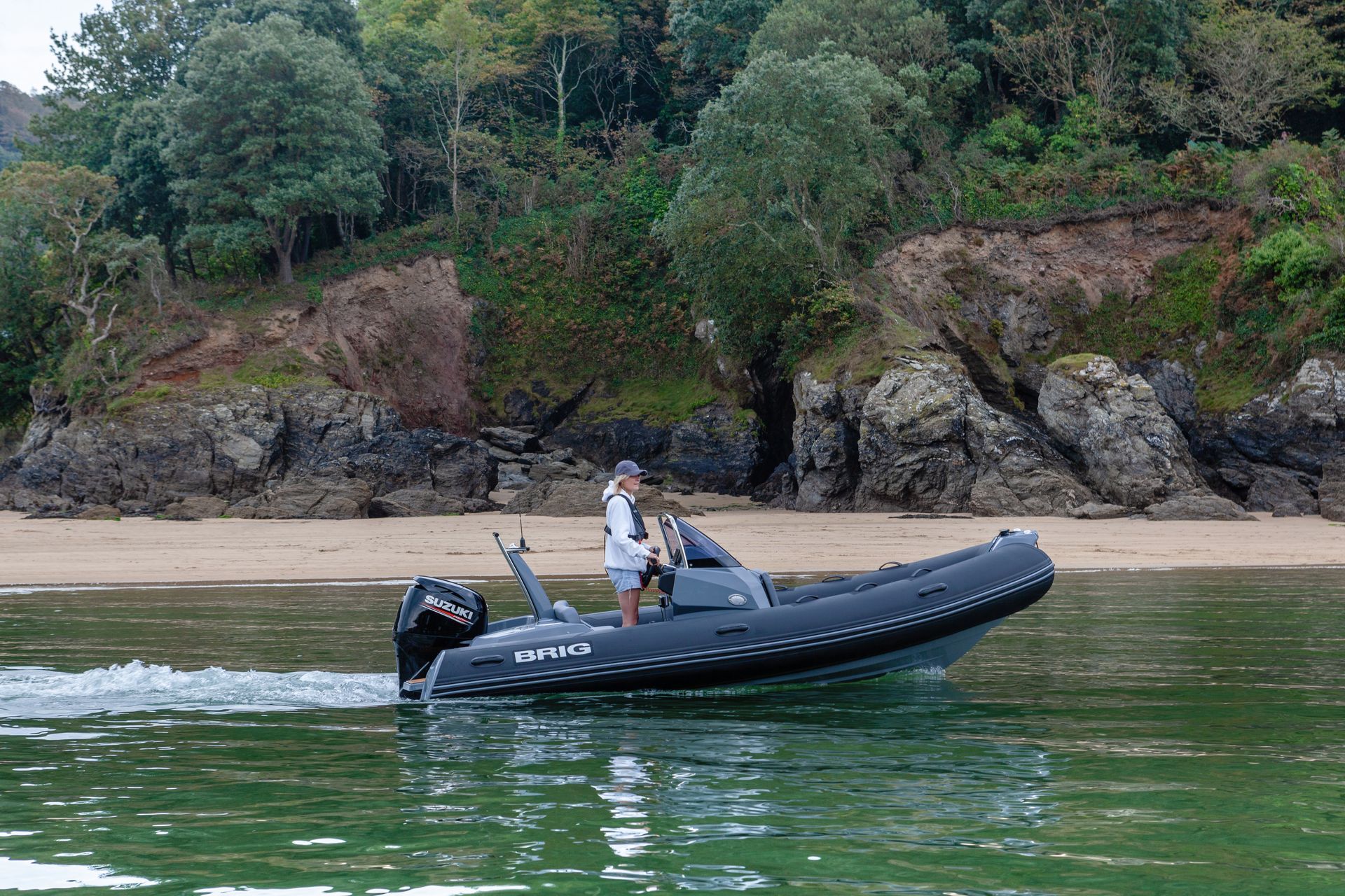 Person on a black inflatable boat near a rocky beach and green shoreline