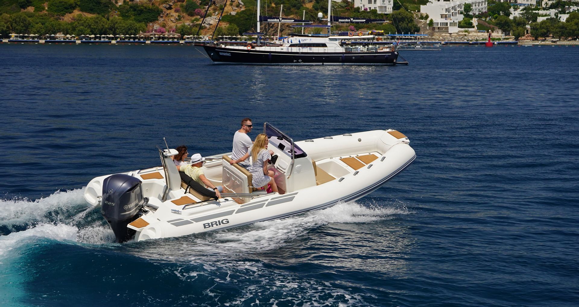 White inflatable boat with passengers speeding across blue water near a rocky shoreline
