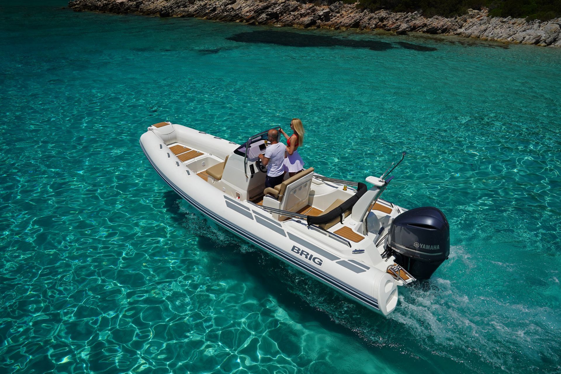 Two people ride a white motorboat on bright turquoise water.