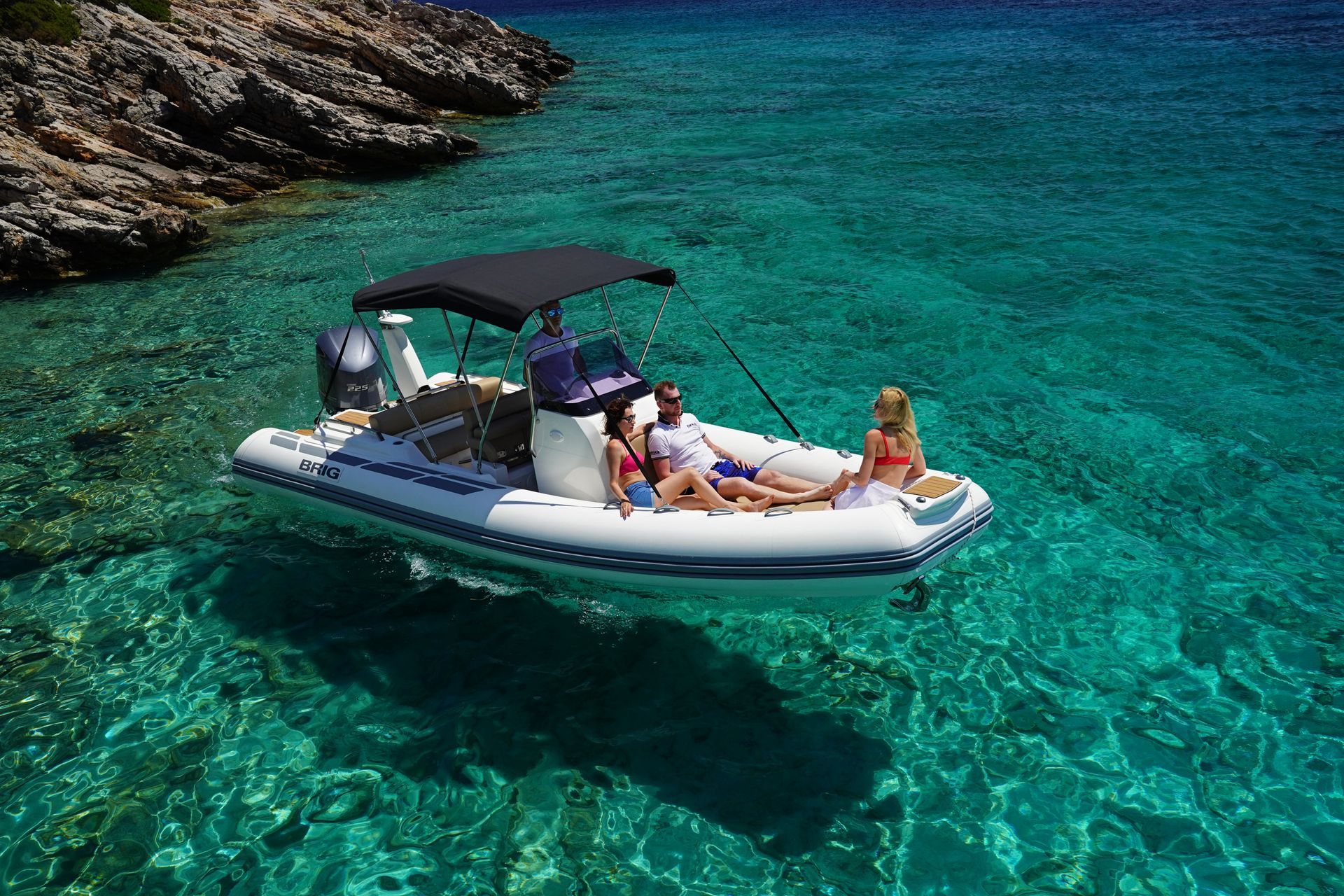 Inflatable boat with people floating on clear turquoise water beside rocky shore