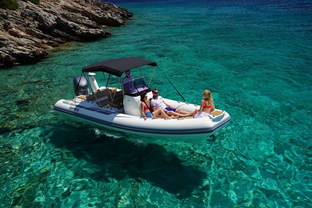 People relaxing on a small boat in clear turquoise water near rocky shore