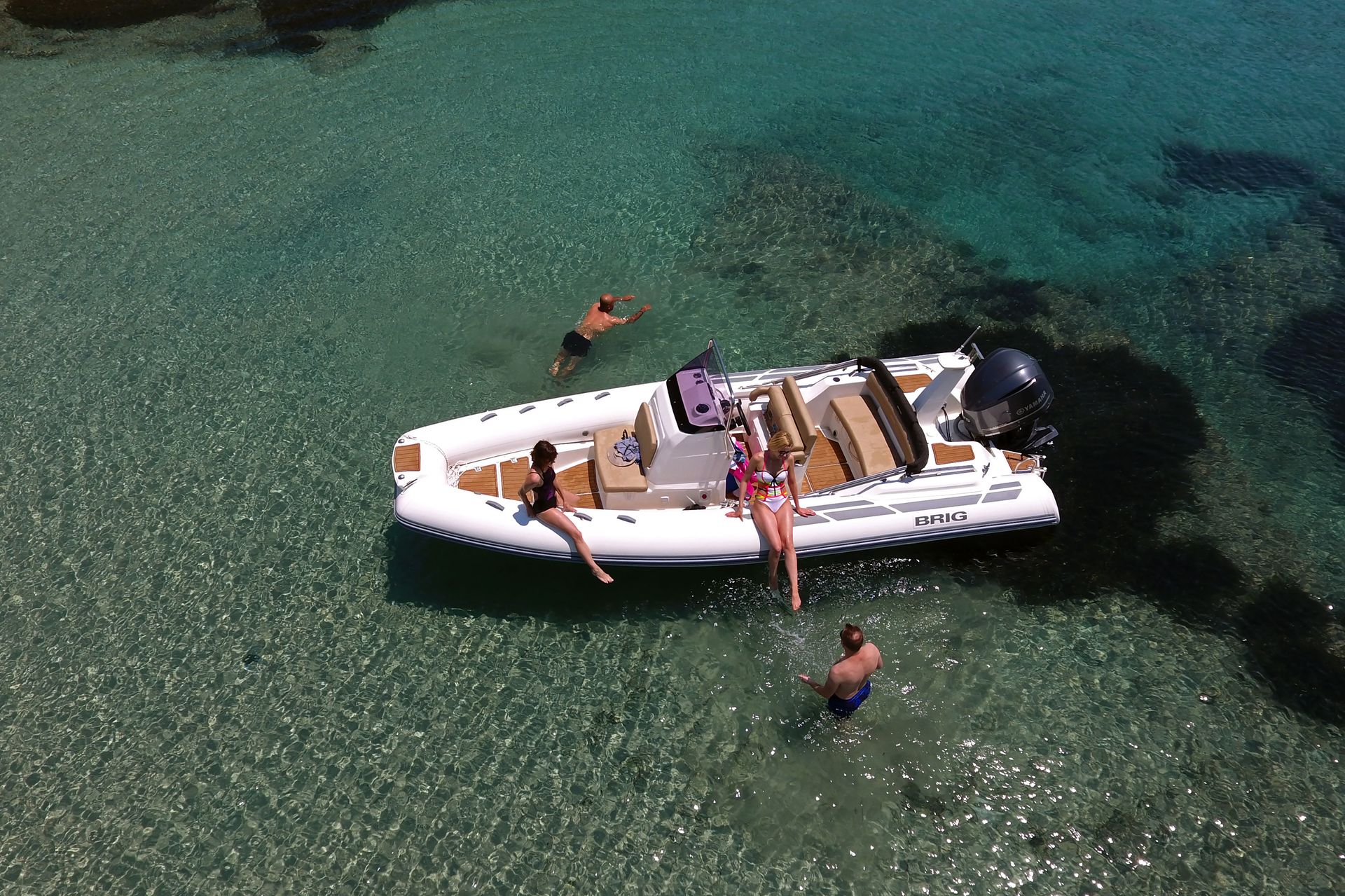 People on a white boat in clear turquoise water, with swimmers nearby.