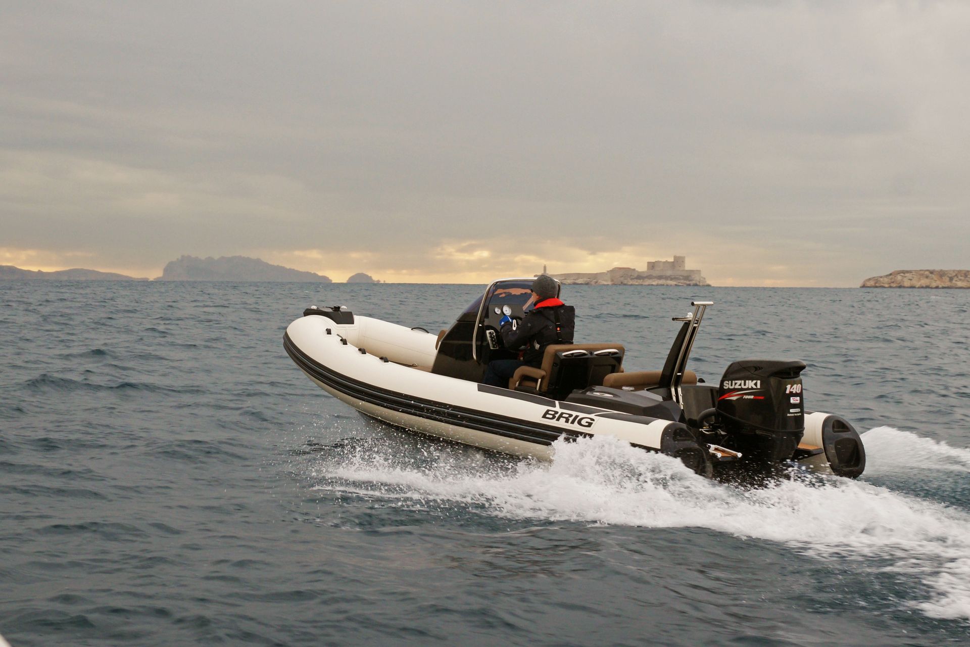Inflatable motorboat speeding across choppy sea under a cloudy sky, with distant ships on the horizon