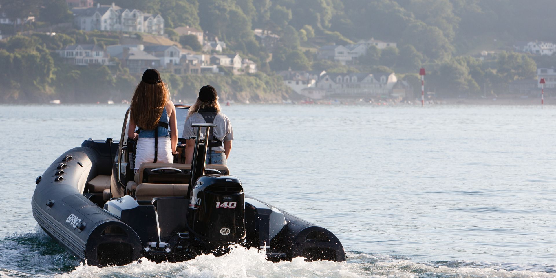 Two people on a black inflatable boat on calm water near a hazy coastline