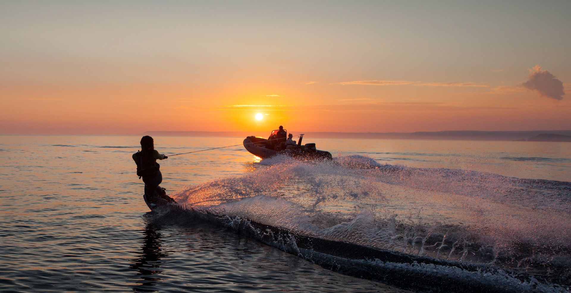 Jet ski speeding across calm water at sunset, spraying a silhouetted rider