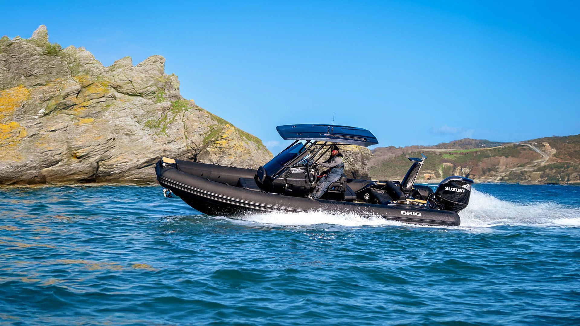 Black inflatable speedboat racing across blue water near rocky coastline under a clear sky