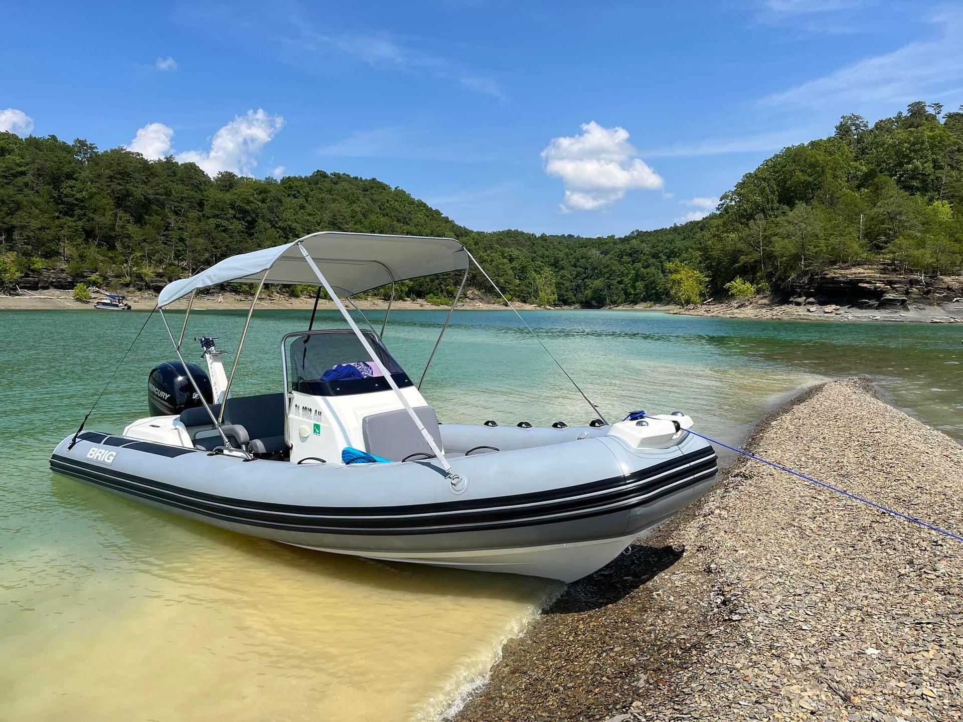 White inflatable boat on clear tropical water near a sandy shore with trees and blue sky