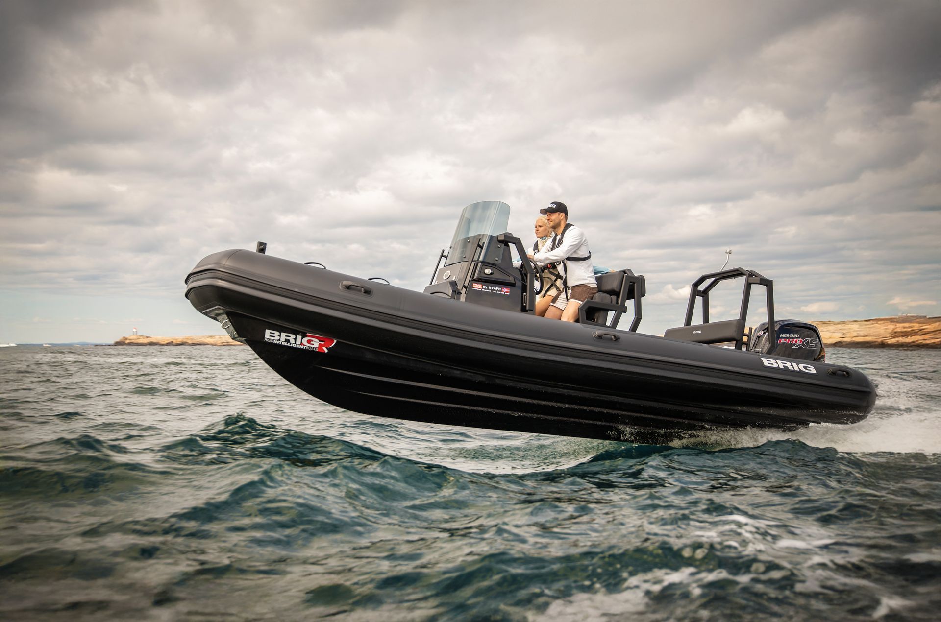 Black motorboat with two people speeding across choppy water under a cloudy sky