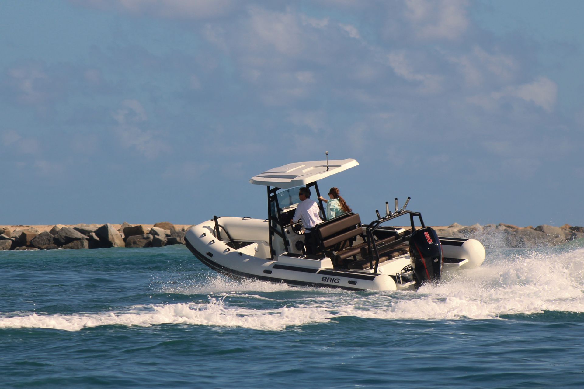 Small motorboat speeding across choppy blue water near a rocky shoreline under a cloudy sky