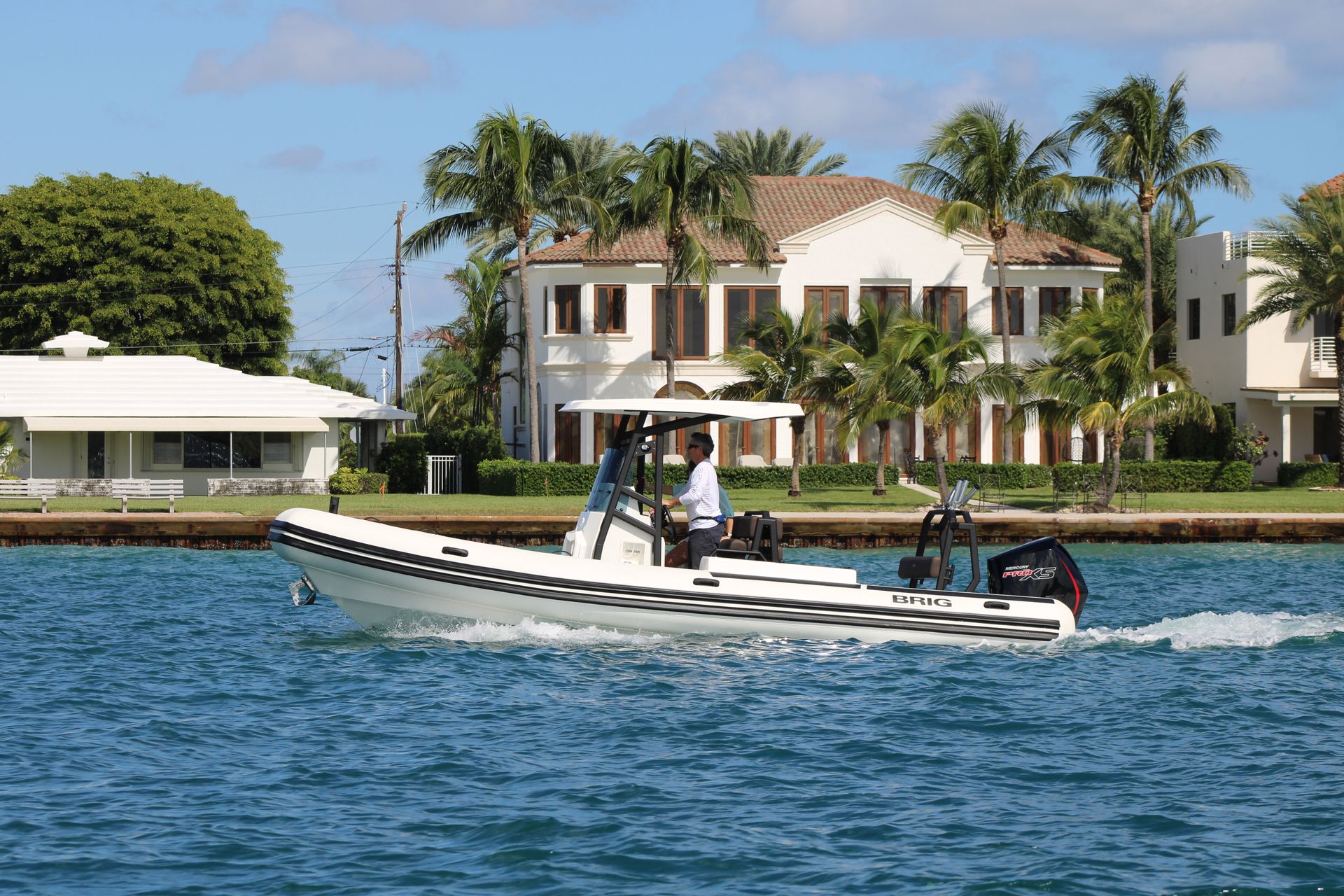 Motorboat on blue water in front of a waterfront mansion with palm trees