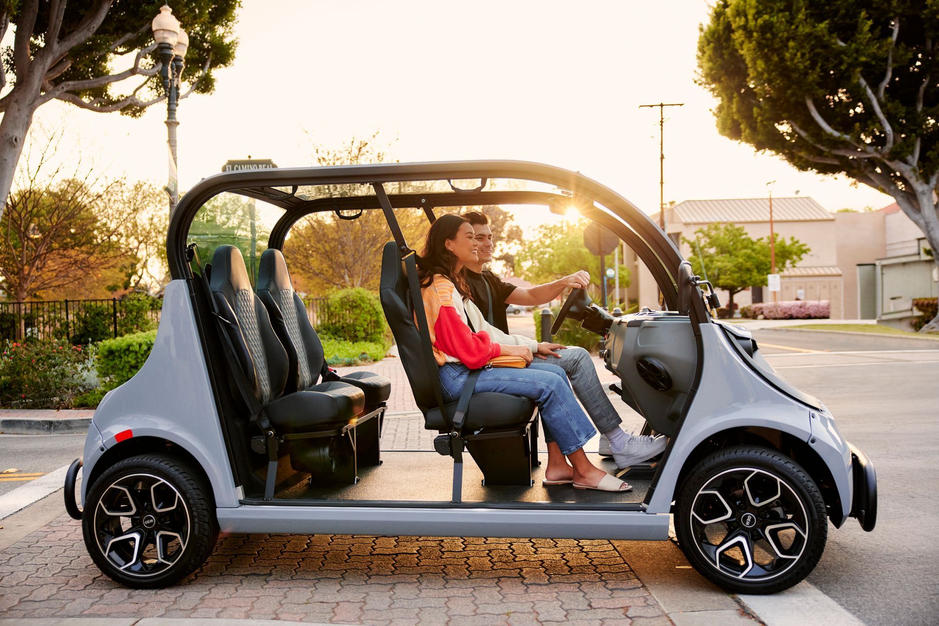 Two people riding in a small open electric car on a sunny street, side view