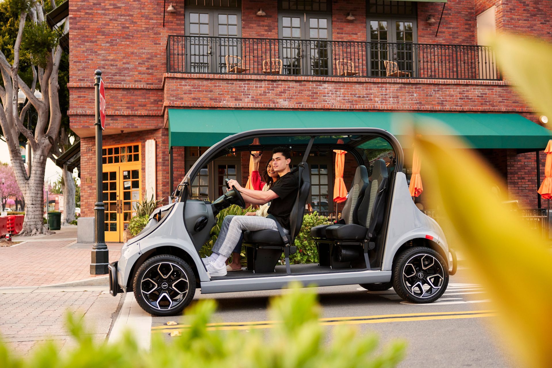 Person sitting in a small gray electric cart on a city street beside a brick building and green awning