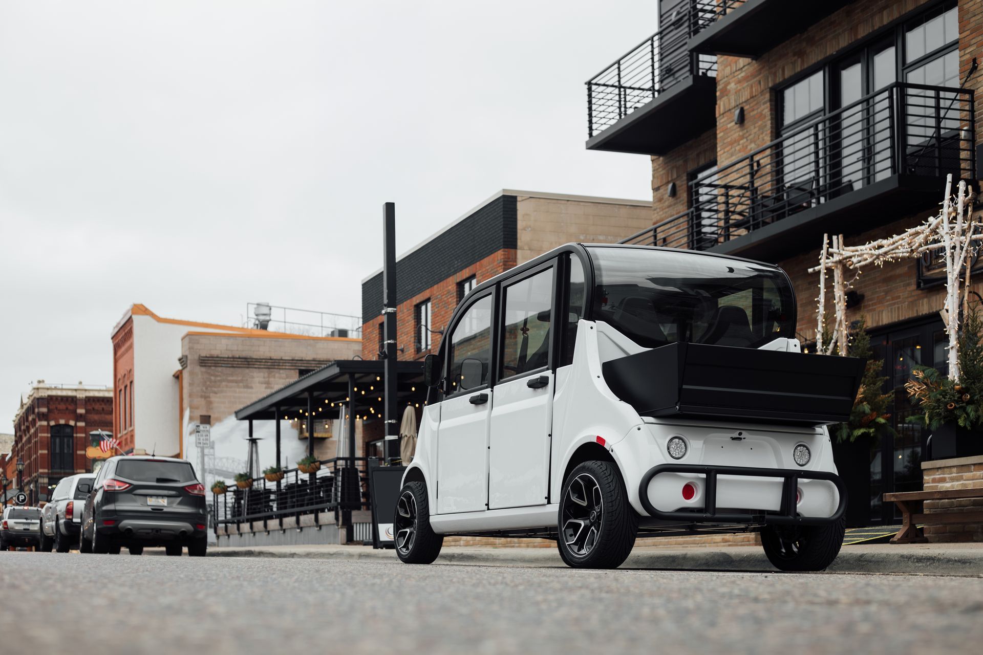 White utility cart on a city street with apartment buildings and parked vehicles in the background
