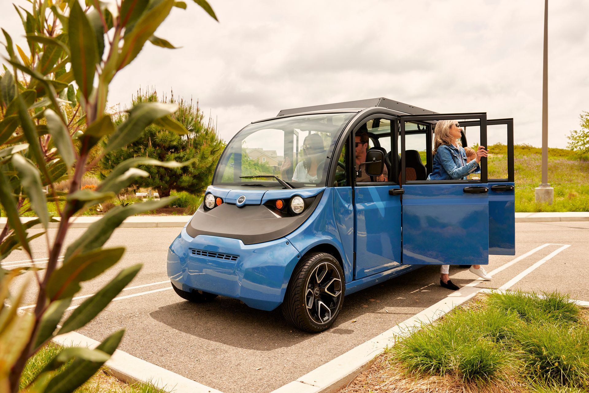 Blue electric shuttle van parked outdoors with its side door open on a sunny roadside