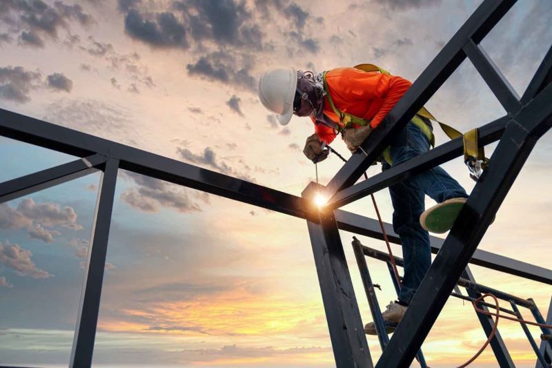 A construction worker is welding a metal structure on top of a building.