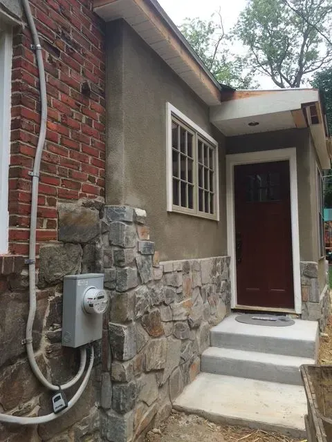 Exterior view of a house entrance with stone veneer, concrete steps, and a brown door.