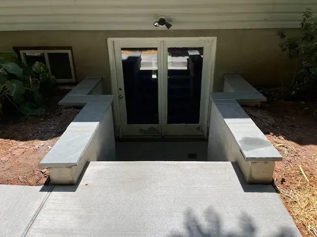 Concrete steps leading to a basement entrance with double doors, flanked by short walls.