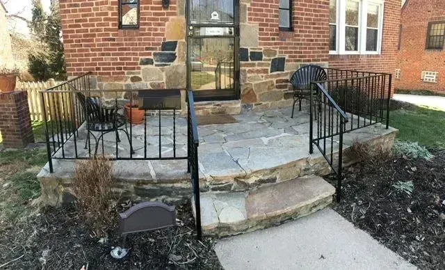 Stone and brick house entryway with wrought iron railings, small chairs, and a door.