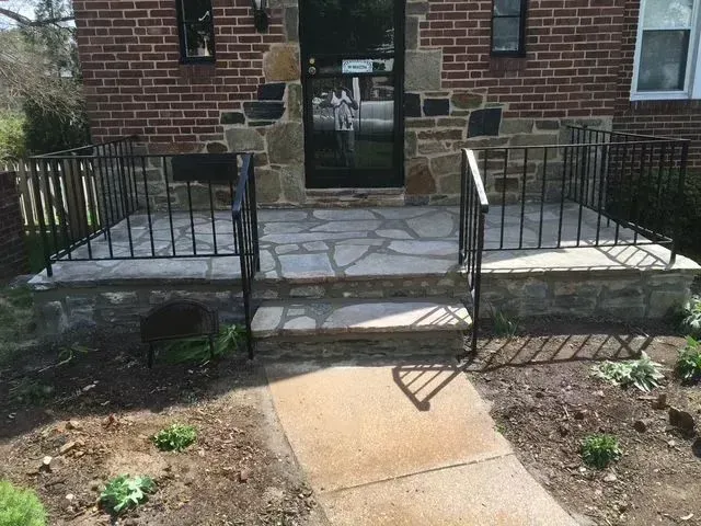 A stone-paved porch with black railings and steps leading to a brick building entrance.