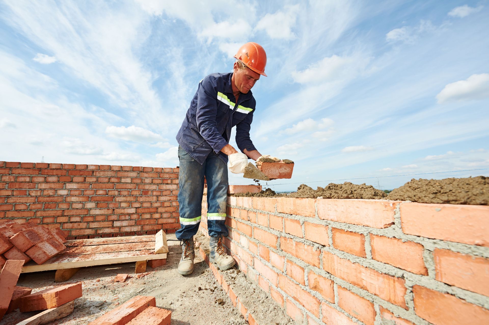 Bricklayer wearing a hard hat, laying bricks on a sunny day.