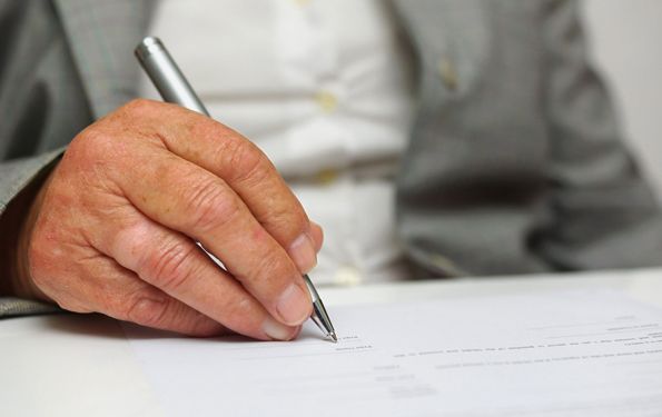 An old man is signing on a piece of paper with a pen.