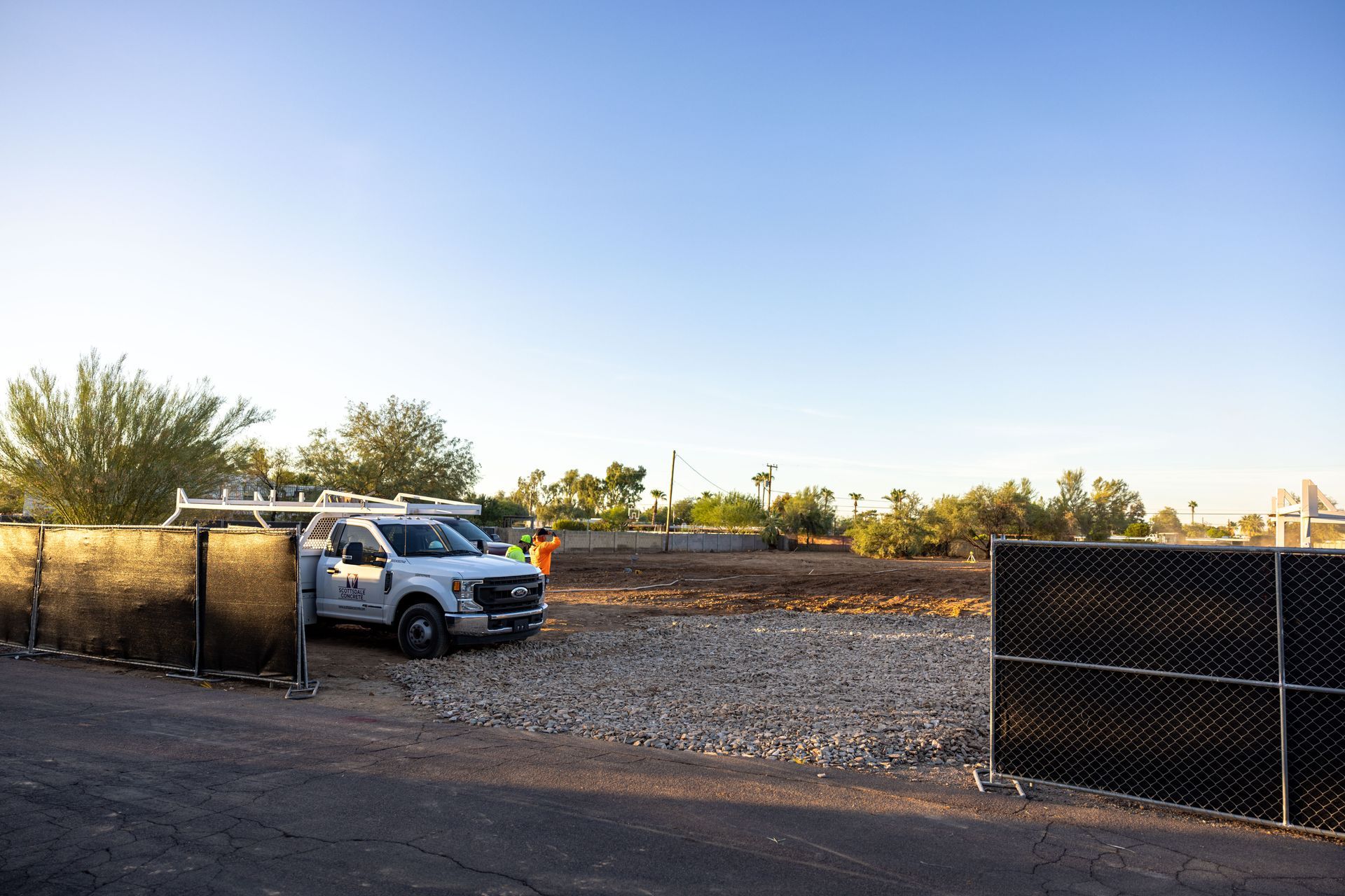 White pickup truck parked by a chain-link gate in a gravel lot at sunset