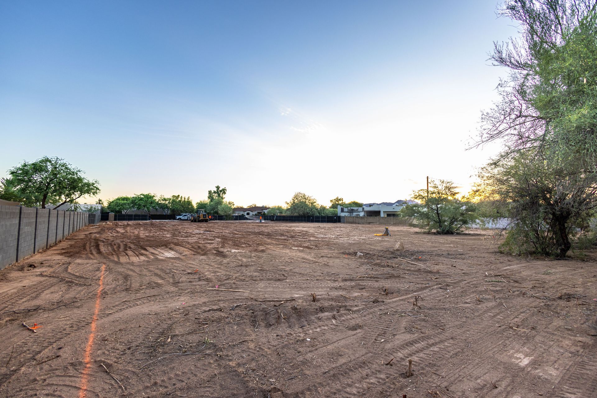 Empty dirt lot at sunset with trees and a fence along the left side