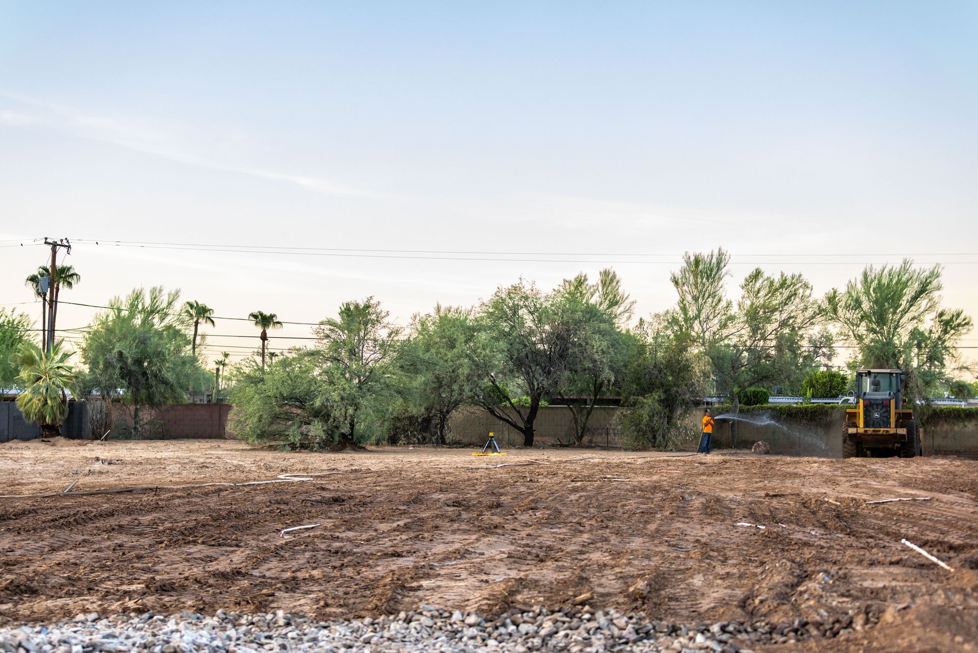 Wide dirt field with trees and a yellow excavator under a clear sky