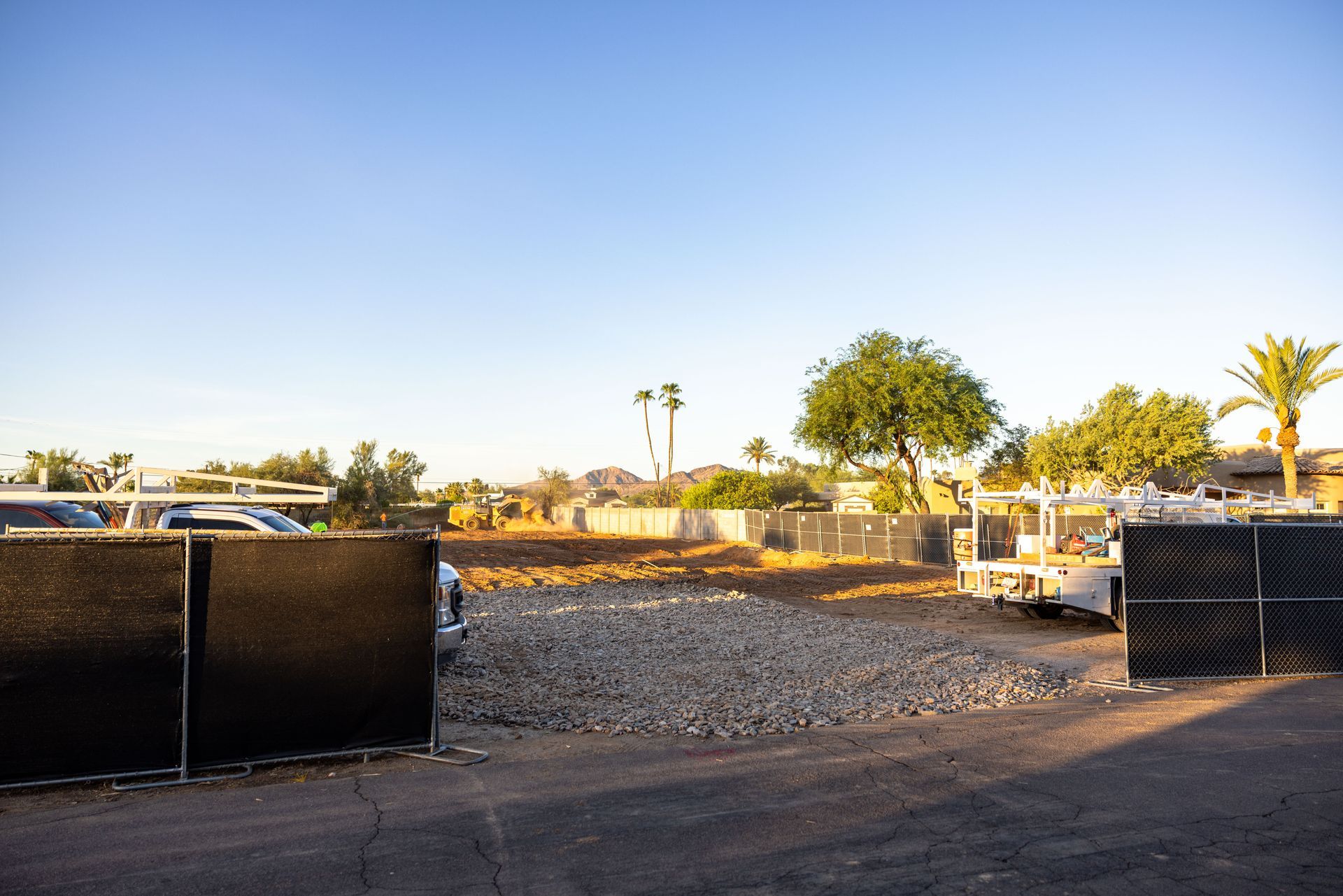 Gravel lot with black barriers, trees, and parked vehicles under a clear blue sky at sunset