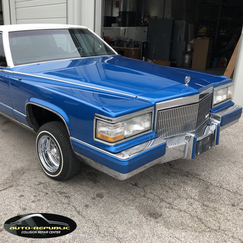 A blue and white cadillac is parked in front of a garage.