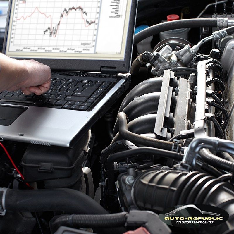A person is working on a car engine with a laptop