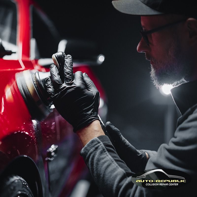 A man wearing black gloves is polishing a red car