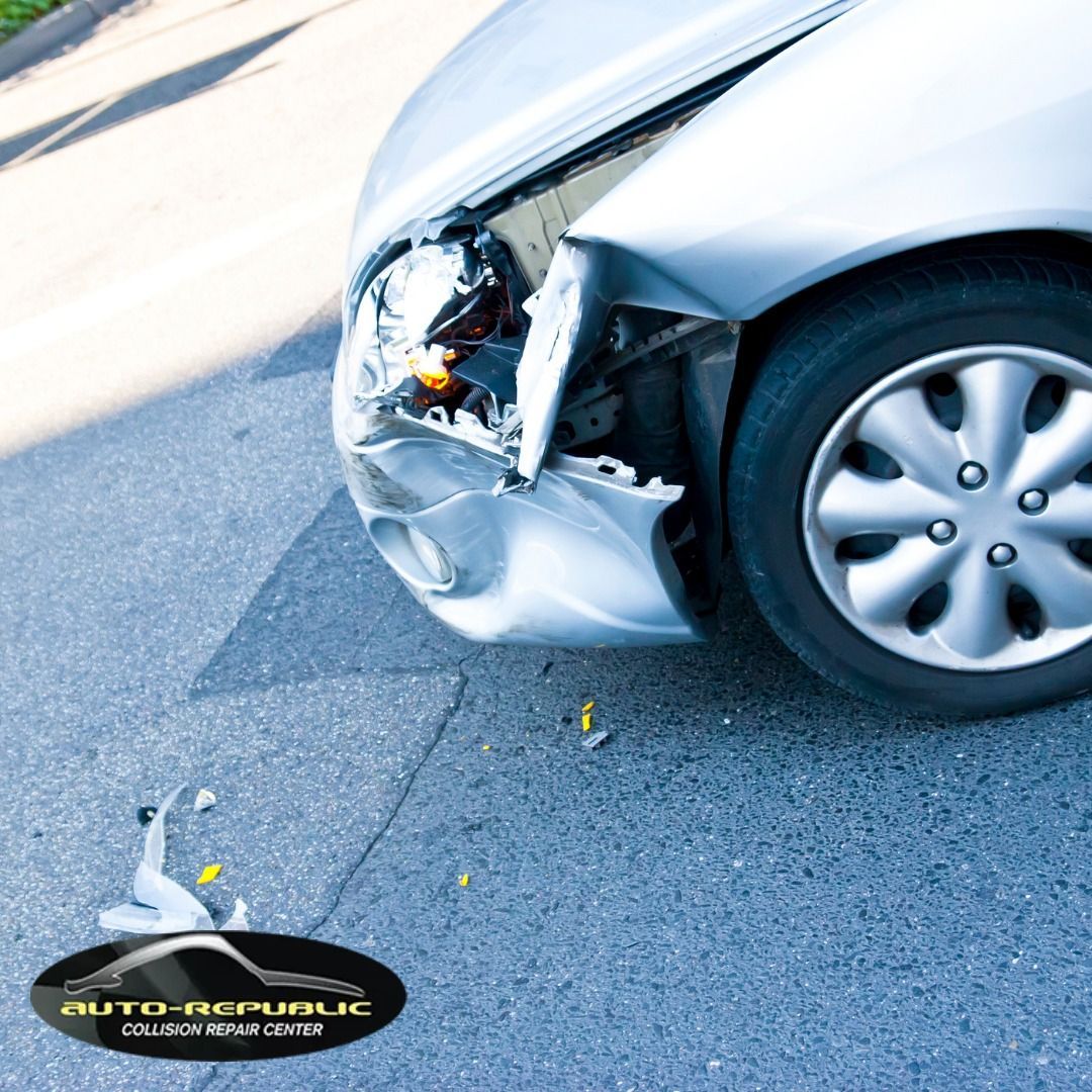 A silver car with a damaged bumper is parked on the side of the road