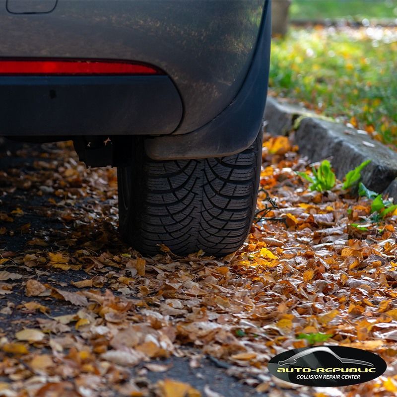 A car is parked on a sidewalk with leaves on the ground