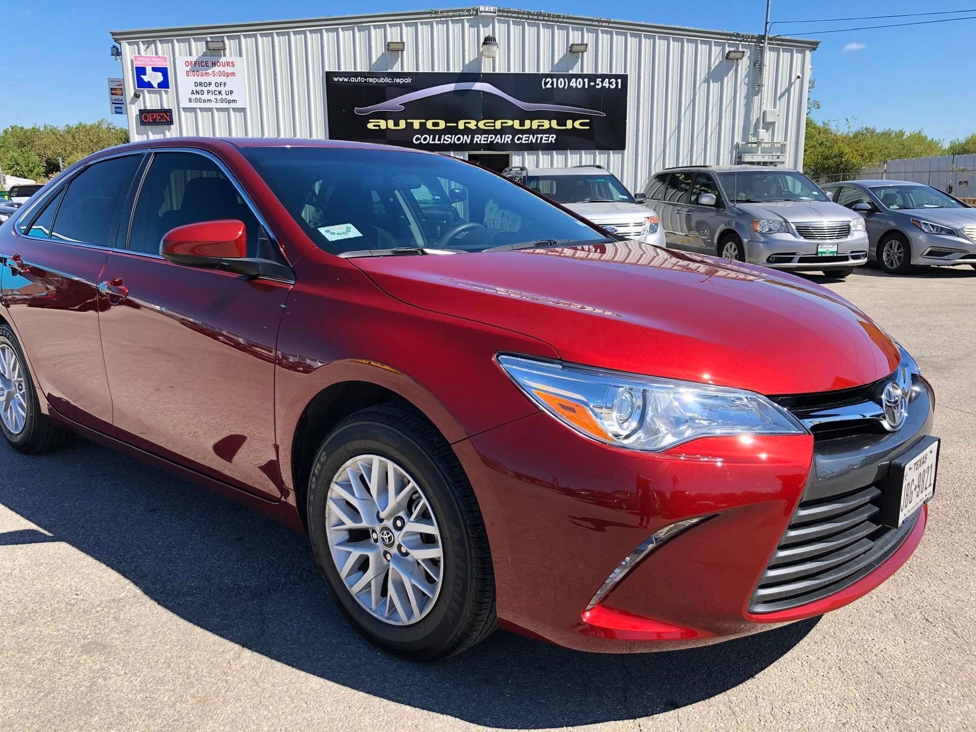 A red toyota camry is parked in front of a car dealership.
