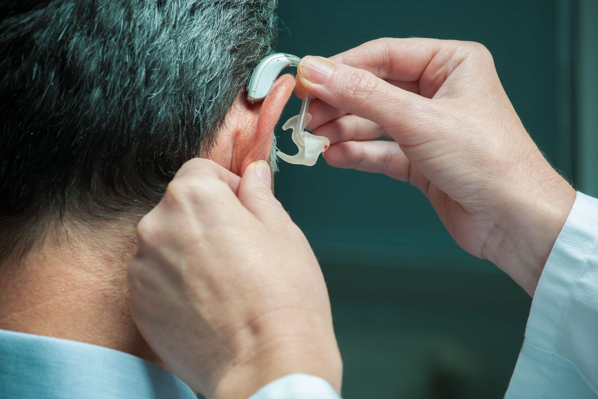 Person's ear with a hearing aid being fitted by someone else. Close up view.