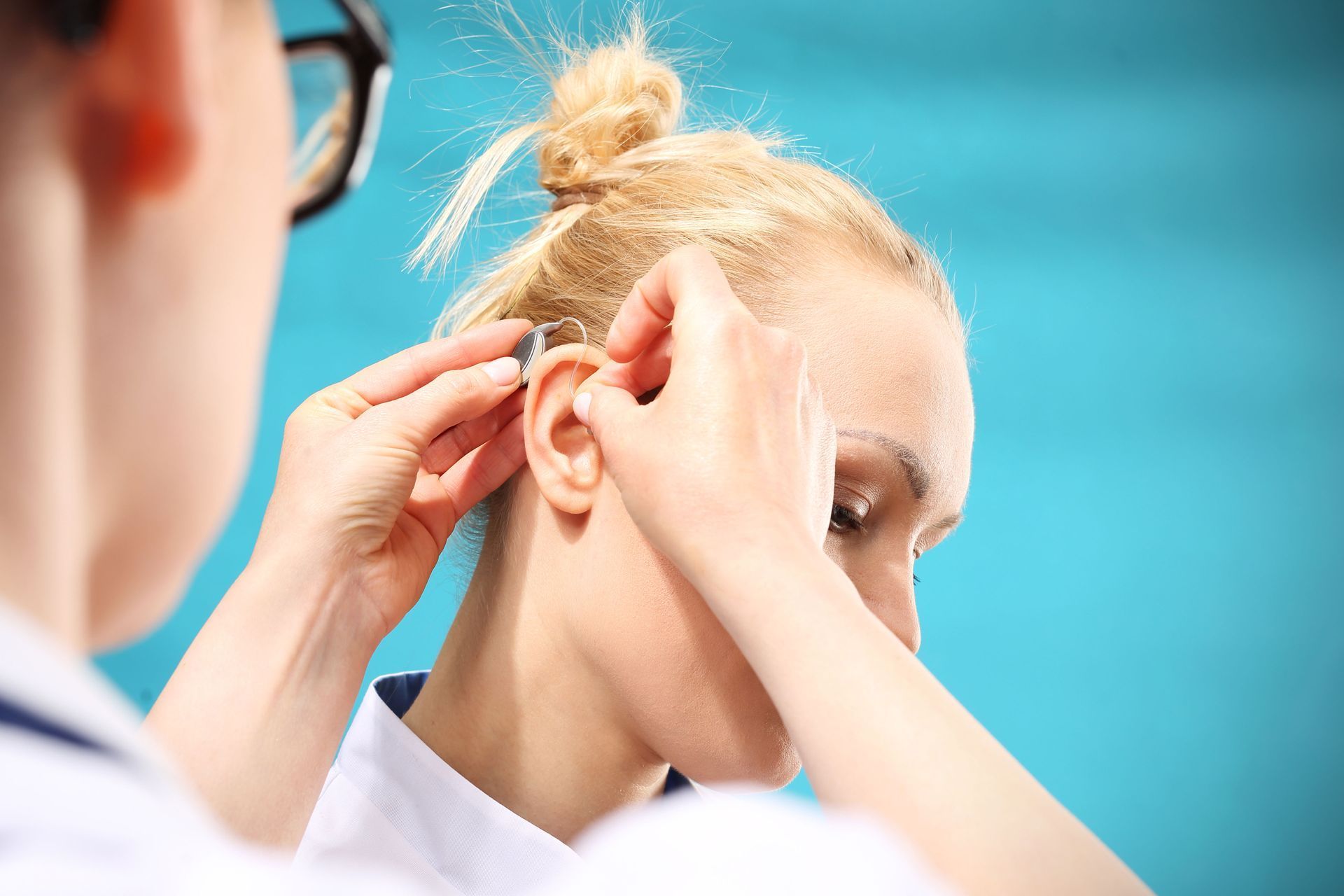 A person placing a hearing aid in another person’s ear. Blue background.