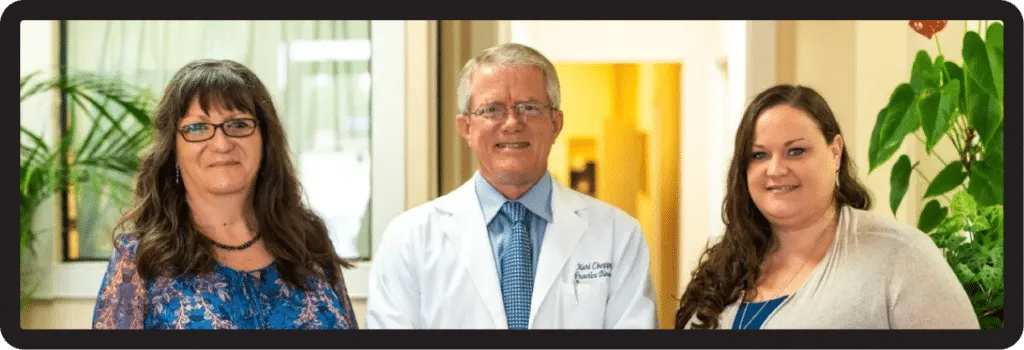 Three people posing for a photo. A doctor in a white coat stands between two women.