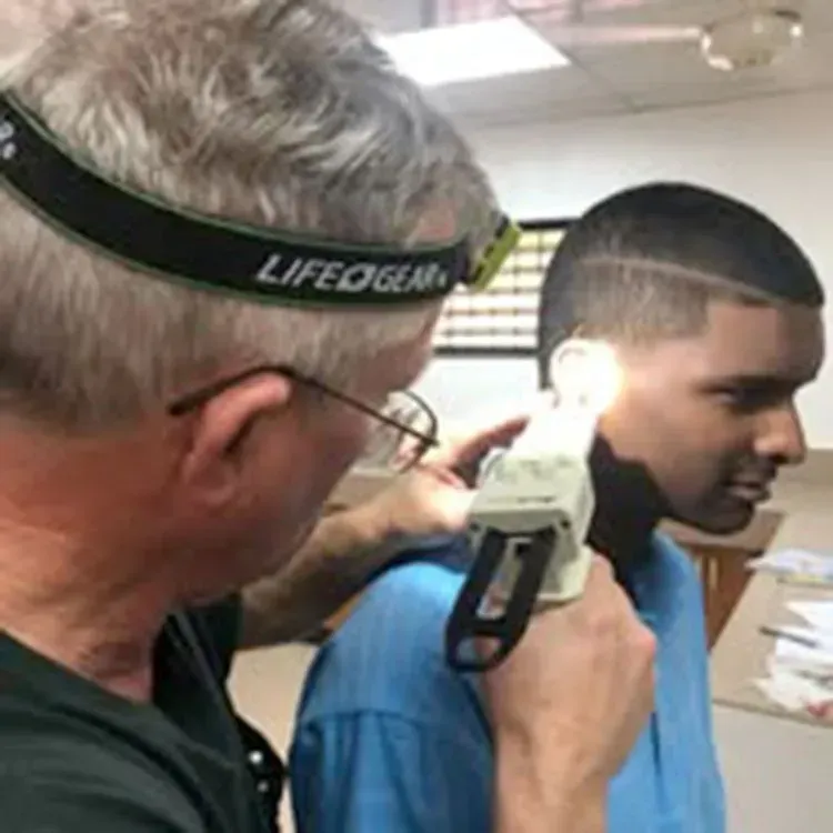 Man using an otoscope to examine a person's ear. They are indoors.