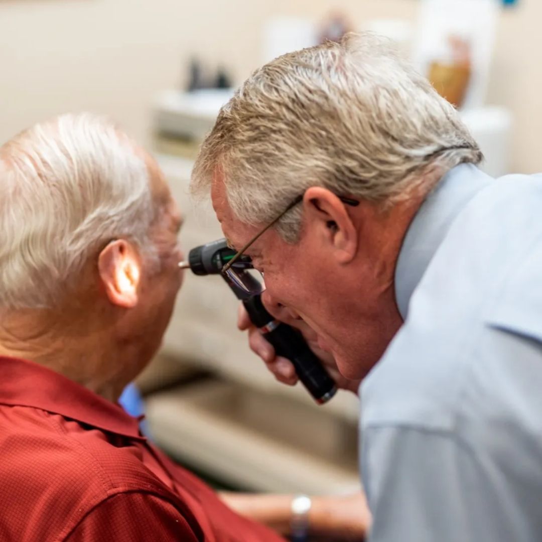 Doctor examining patient's ear with an otoscope in a medical office.