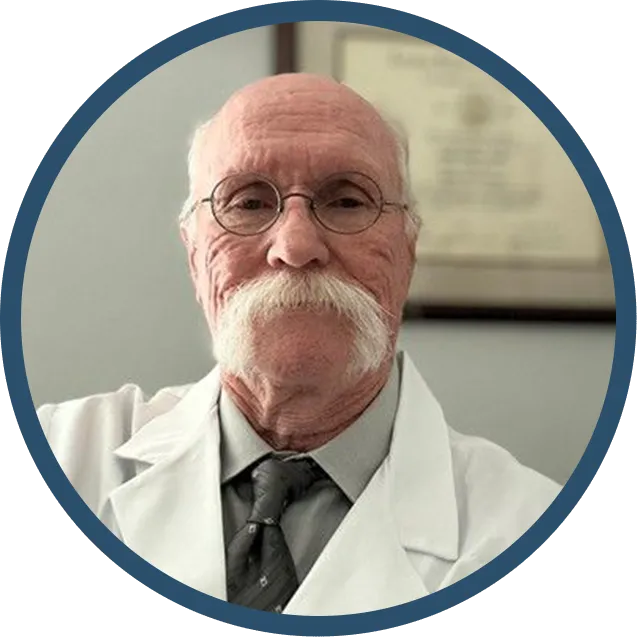 Older man in white lab coat, glasses, and large white mustache, likely a doctor.